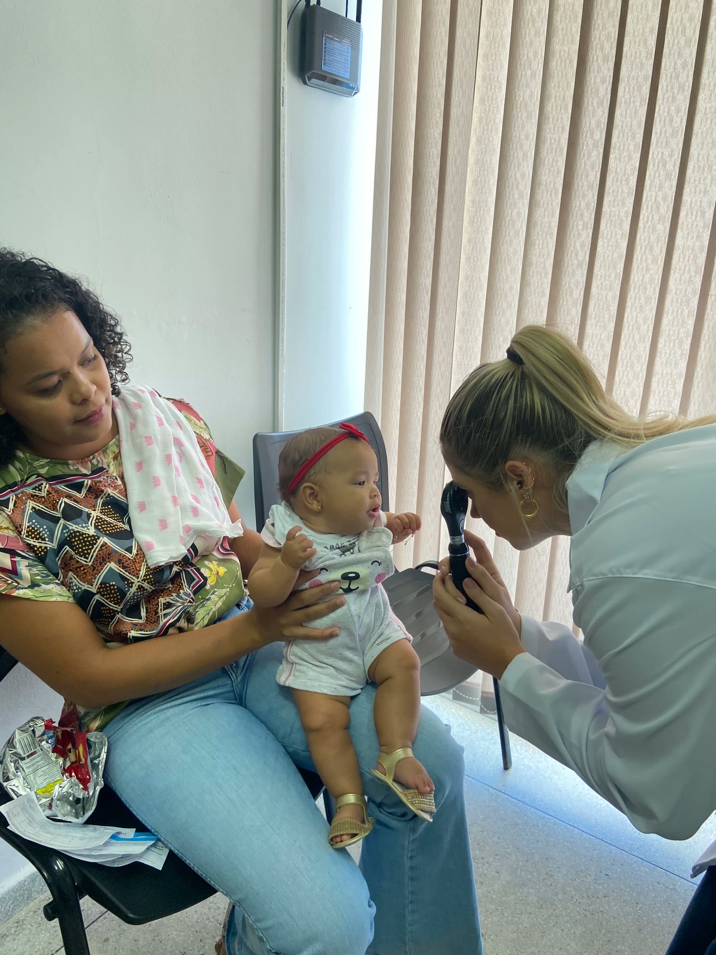 Oftalmologista realiza teste do olhinho em bebê no colo da mãe durante mutirão