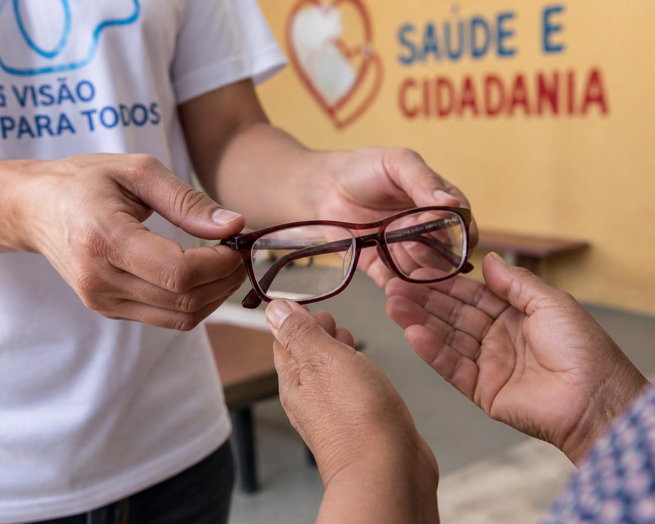 Mãos entregando um par de óculos a outra pessoa durante mutirão do Instituto